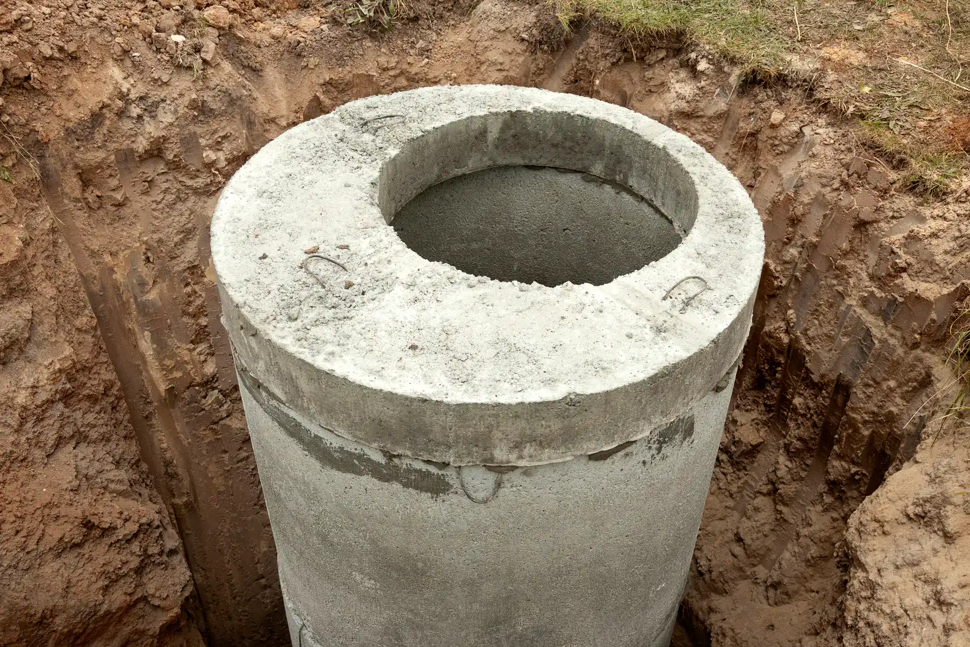 A concrete well ring stands upright in a dirt pit, commonly used for cesspool service in Suffolk County, NY.