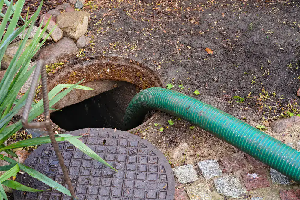 A green hose feeds into an open manhole outdoors, showing a drain cleaning Suffolk County, NY service.