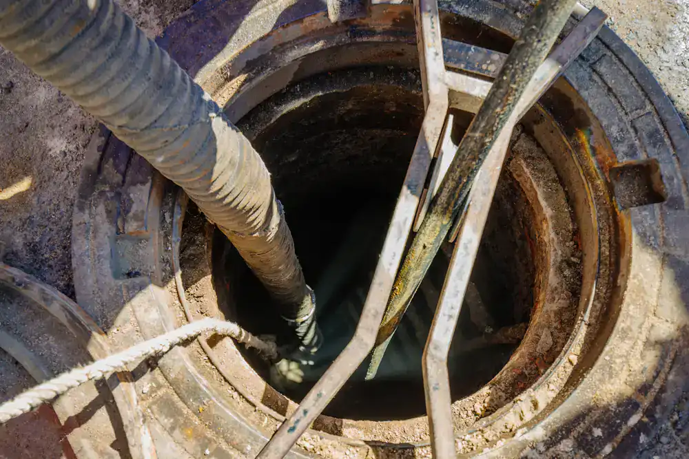 Open manhole with hoses and pipes inserted, showing Cesspool Service Suffolk County work in progress.