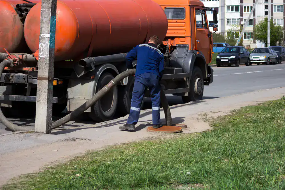 A worker in a blue uniform uses a hose from an orange tanker for drain cleaning in Suffolk County, NY.