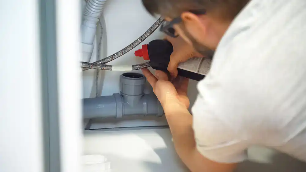 A technician cleans a drain under a kitchen sink, adjusting pipes during Suffolk County service.