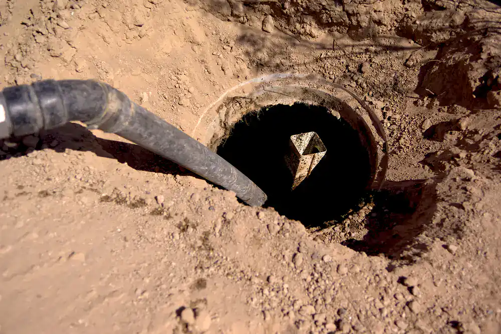 A black pipe entering a round hole in dry soil, typical for cesspool service in Suffolk County, NY.