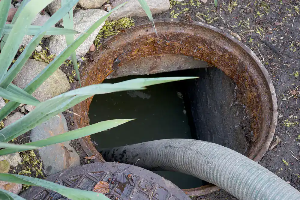 A hose goes into a rusty manhole, illustrating drain cleaning Suffolk County services in action.