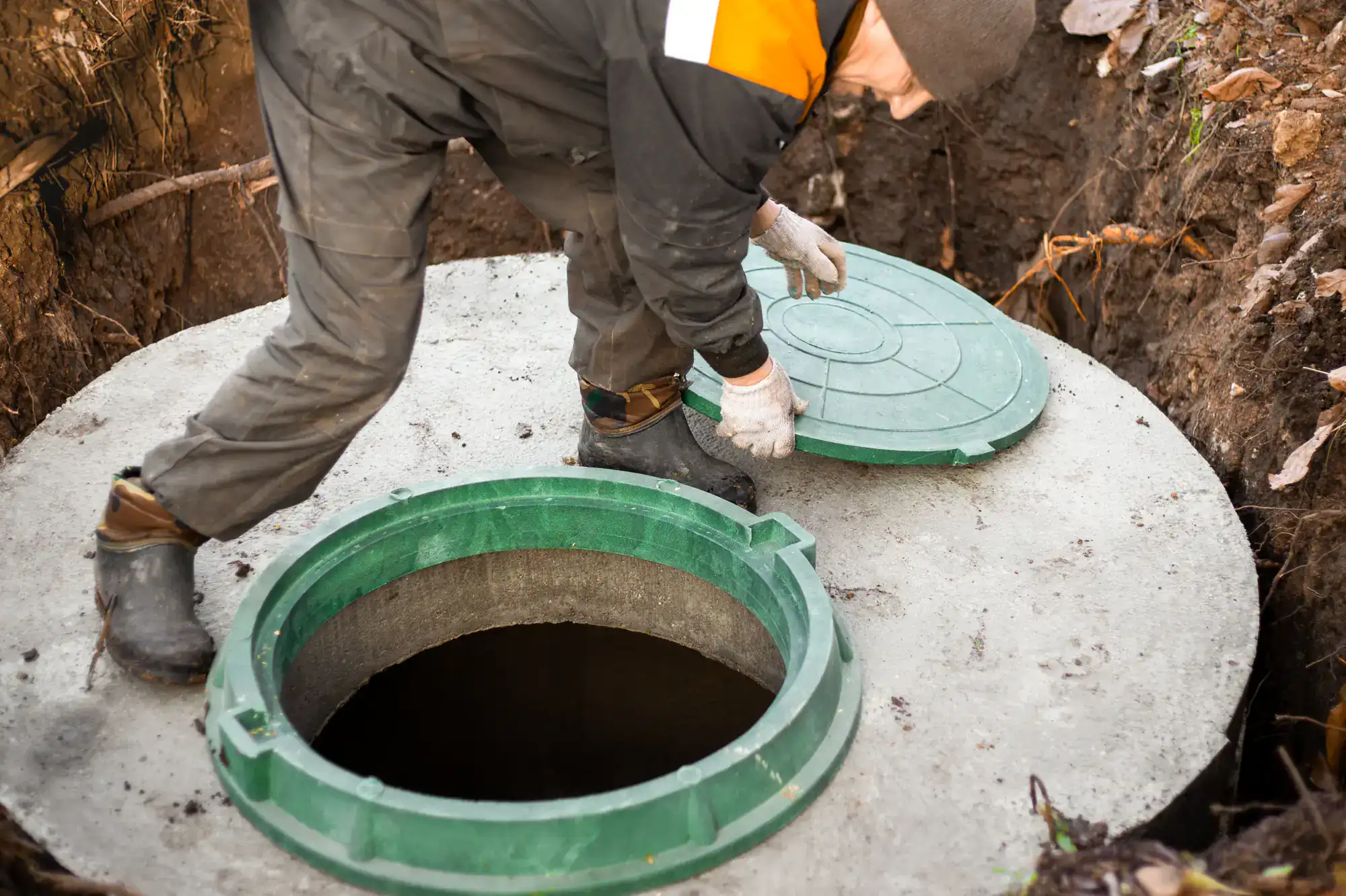 A worker in uniform lifts a green septic tank lid during septic services in Suffolk County.
